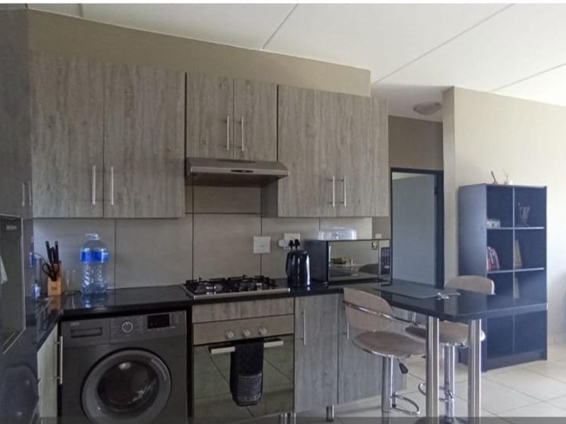 Open-plan kitchen featuring modern wood-grain cabinetry, granite countertops, gas hob, built-in oven, and integrated laundry facilities, flowing into the living area.