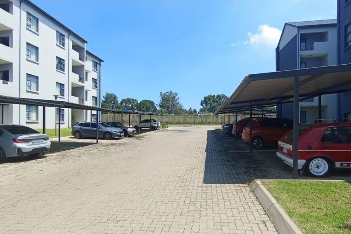 Exterior view of the apartment complex featuring paved parking areas with covered carports and landscaped grounds.