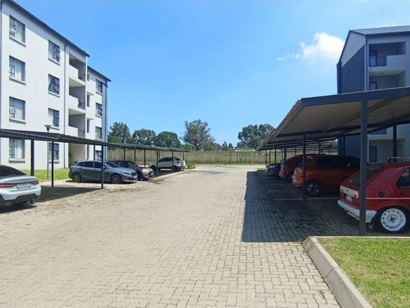 Exterior view of the apartment complex featuring paved parking areas with covered carports and landscaped grounds.