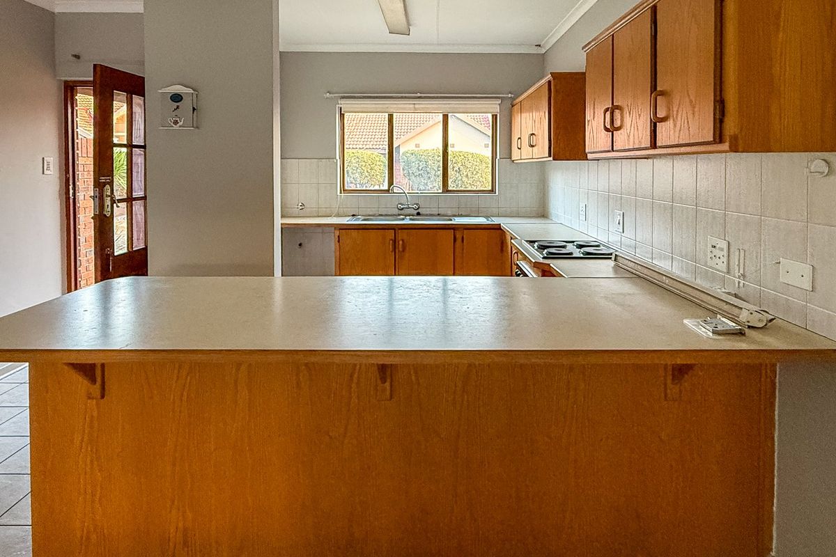 A functional kitchen featuring wooden cabinetry, laminate countertops, a built-in electric hob, and a double basin sink with tiled backsplash.