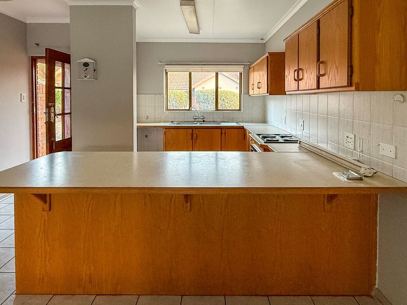A functional kitchen featuring wooden cabinetry, laminate countertops, a built-in electric hob, and a double basin sink with tiled backsplash.