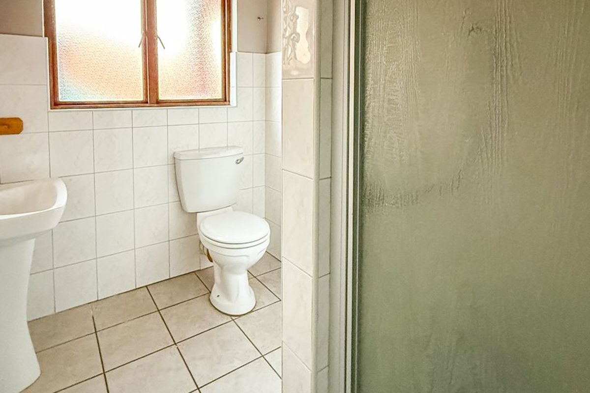 A functional bathroom featuring a pedestal basin, toilet, and a shower enclosure with tiled finishes and an obscured glass window.