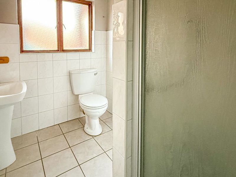 A functional bathroom featuring a pedestal basin, toilet, and a shower enclosure with tiled finishes and an obscured glass window.