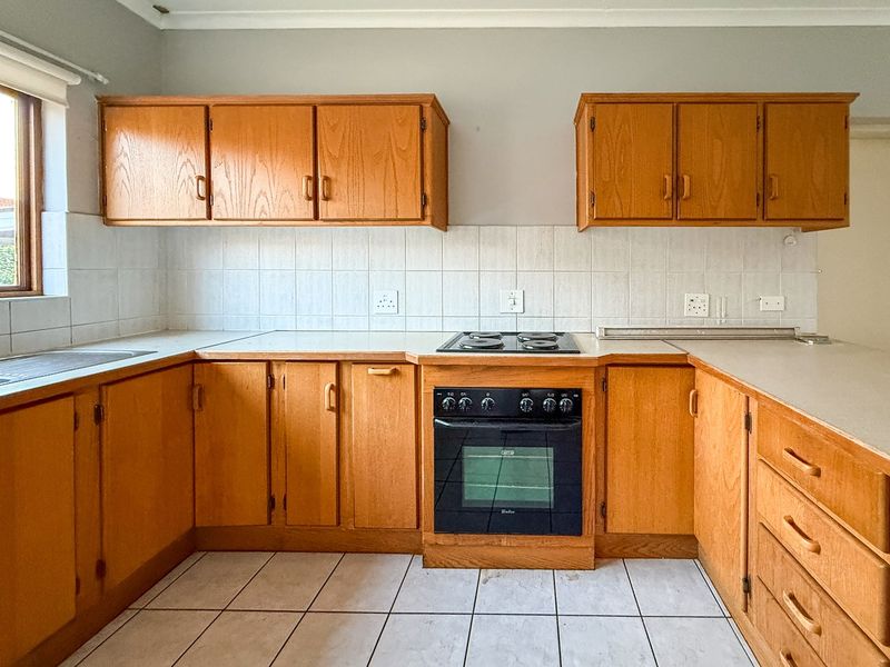 A functional kitchen featuring wooden cabinetry, laminate countertops, a built-in oven, and an electric hob with tiled backsplash and flooring.