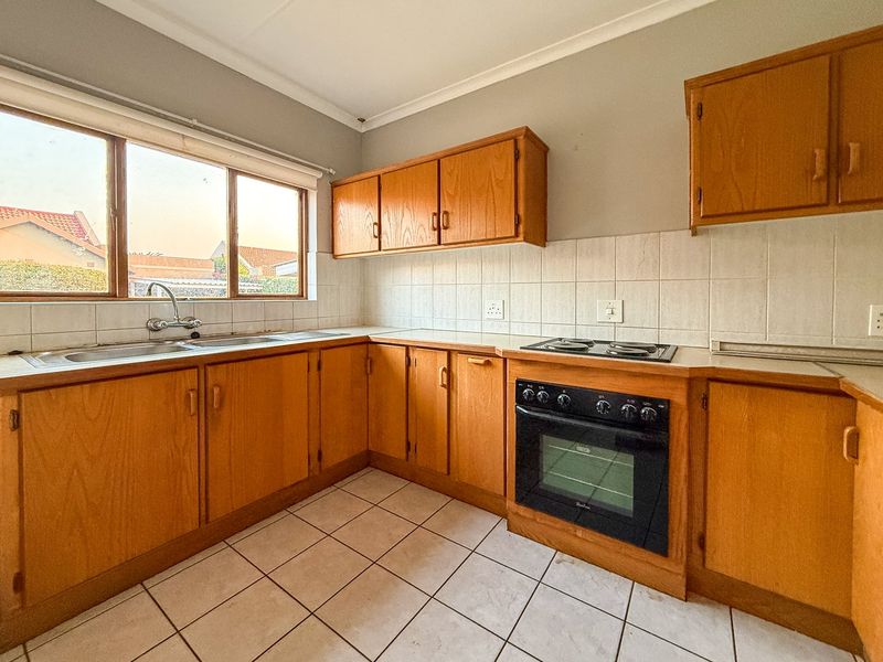 A functional kitchen featuring wooden cabinetry, a built-in oven with electric hob, and a double basin sink with tiled backsplash and flooring.