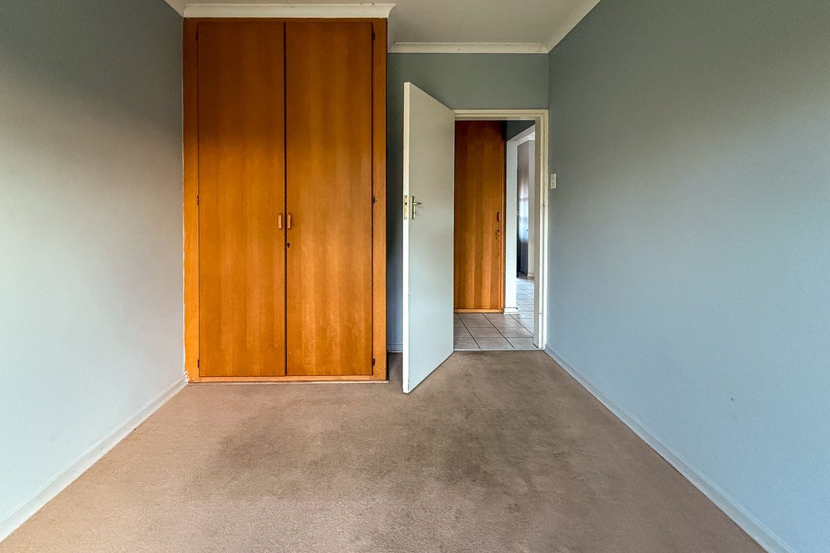 An empty bedroom featuring built-in wooden cupboards, carpeted flooring, and coved cornicing, offering a blank canvas for renovation.