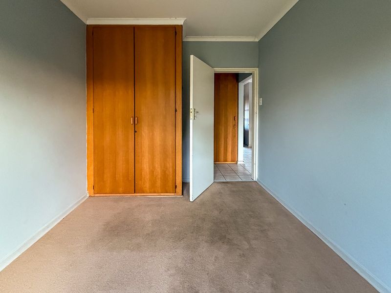 An empty bedroom featuring built-in wooden cupboards, carpeted flooring, and coved cornicing, offering a blank canvas for renovation.