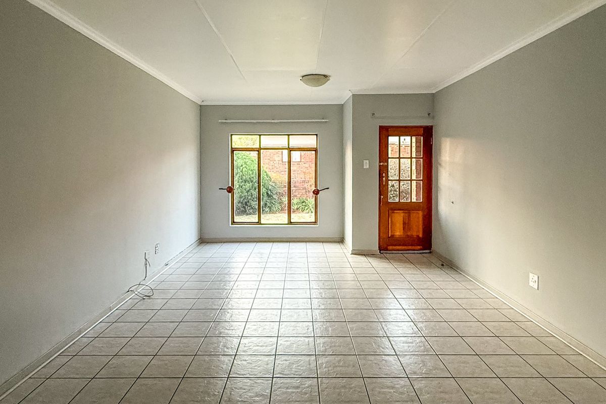 A bright, empty living room featuring neutral walls, ceramic tile flooring, and a classic timber-framed glass door leading to the exterior.