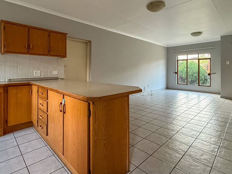Spacious open-plan living and kitchen area featuring tiled flooring, built-in wooden cabinetry, and direct access to the exterior through a timber-framed glass door.