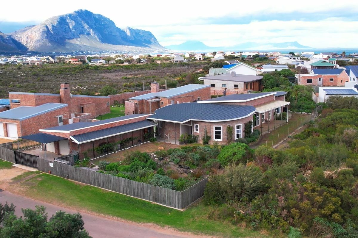 Aerial view of a brick residential property featuring a metal roof, attached garage, and landscaped garden, set against a scenic mountain and coastal backdrop.