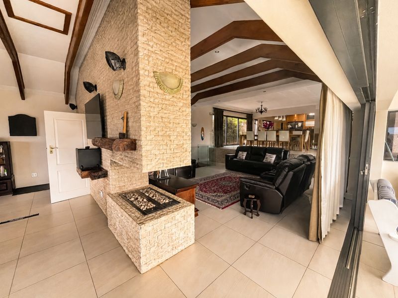Spacious open-plan living area featuring a prominent stone-clad fireplace, exposed timber beams, and large sliding doors leading to outdoor space.