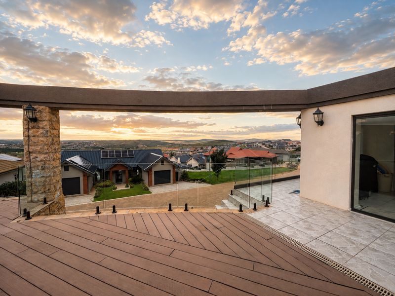 Spacious elevated balcony featuring composite decking, glass balustrades, and stone-clad pillars, offering expansive views over the surrounding residential estate.