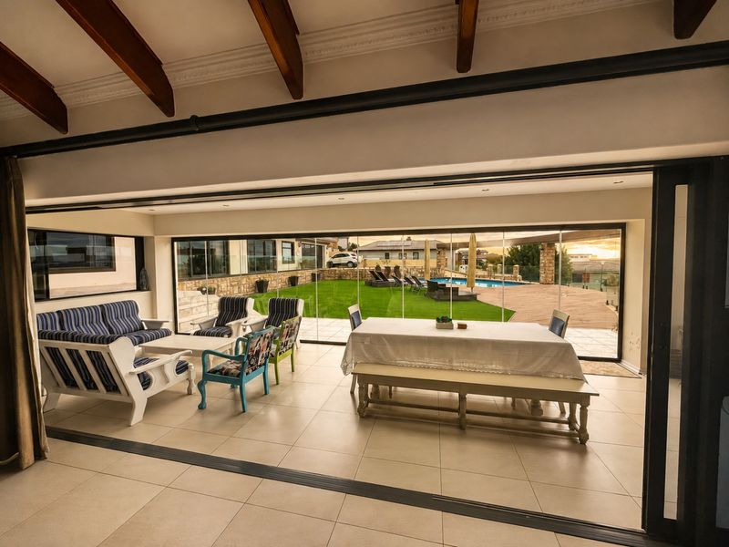 Spacious open-plan living and dining area featuring exposed timber beams, large format floor tiles, and seamless stacking glass doors opening to the garden.