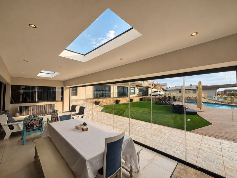 Spacious covered patio featuring large skylights, recessed lighting, and seamless frameless glass doors opening onto a landscaped garden and pool area.