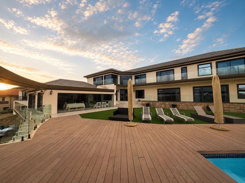 Spacious rear exterior featuring composite decking, a swimming pool, glass balustrades, and a well-maintained artificial lawn against a modern two-story residence.