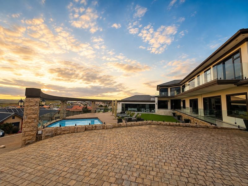 Expansive rear exterior featuring a paved patio, timber decking, swimming pool, and glass balustrades, set against a scenic sunset backdrop.