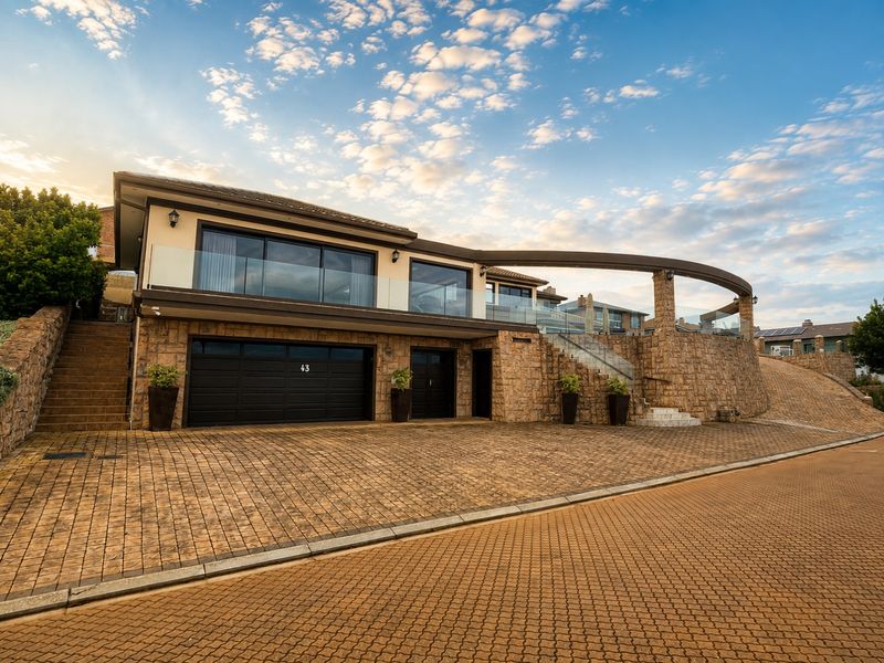 Modern multi-level residence featuring stone cladding, a double garage, paved driveway, and a prominent curved architectural beam with glass balustrades.