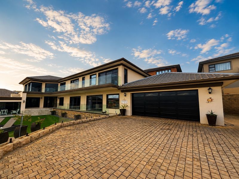 A modern multi-story residential property featuring a paved driveway, double garage, and glass balustrades, showcasing a well-maintained exterior facade.