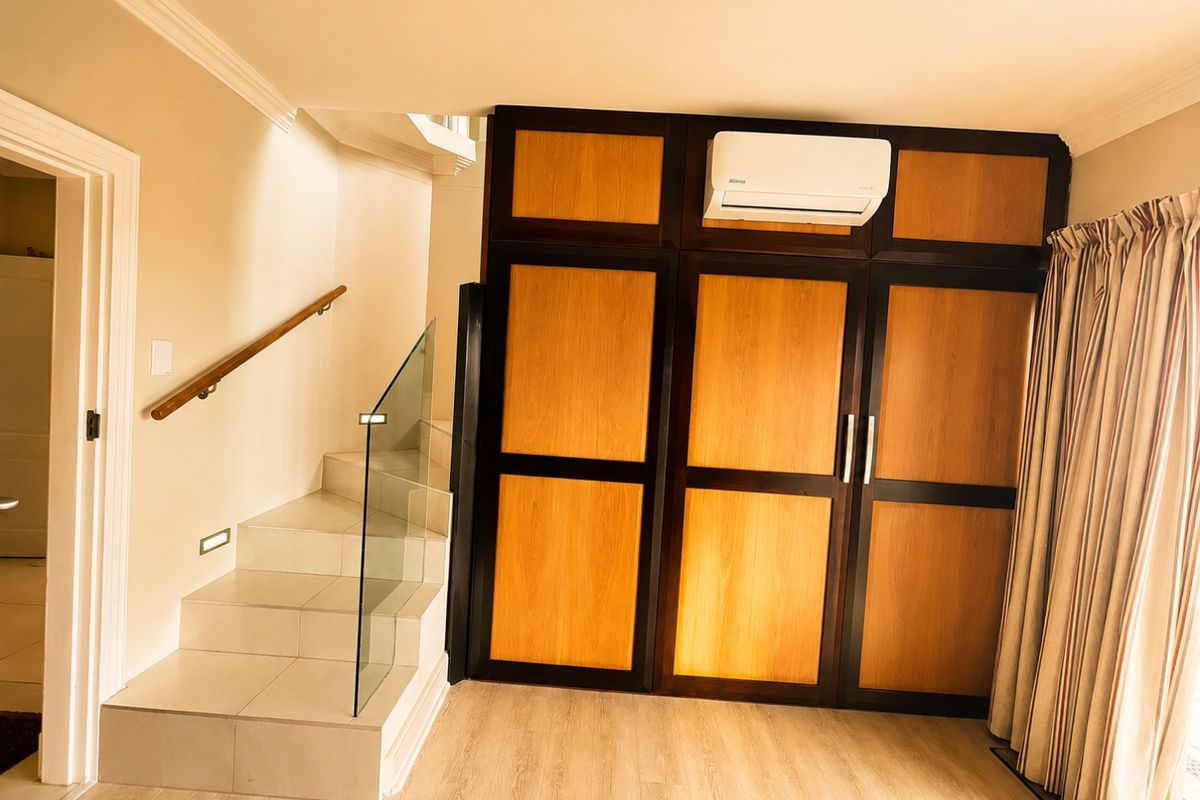 A well-maintained bedroom featuring built-in wooden cabinetry, a modern staircase with a glass balustrade, and a wall-mounted air conditioning unit.