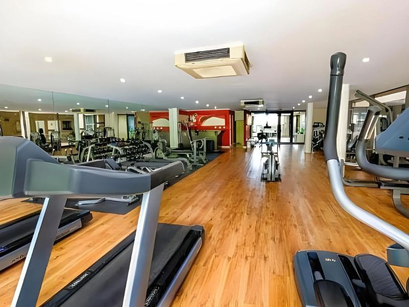 A spacious, well-lit gym facility featuring hardwood flooring, mirrored walls, and integrated ceiling-mounted air conditioning units.