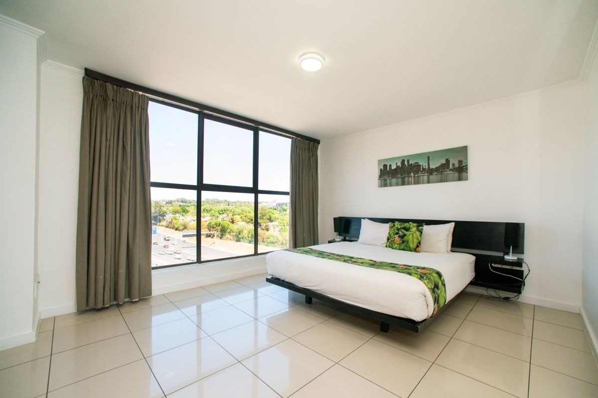A bright bedroom featuring large floor-to-ceiling windows with expansive views, neutral tiled flooring, and a modern built-in headboard.