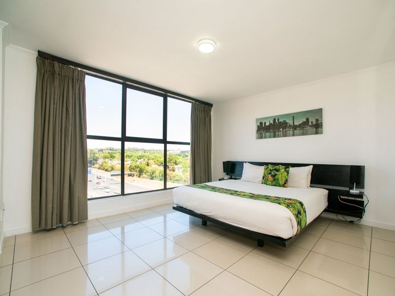 A bright bedroom featuring large floor-to-ceiling windows with expansive views, neutral tiled flooring, and a modern built-in headboard.