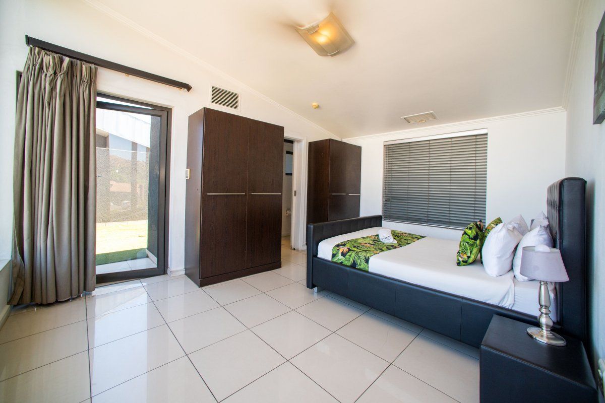 A bright bedroom featuring tiled flooring, built-in cupboards, and a sliding glass door providing direct access to the outdoor area.