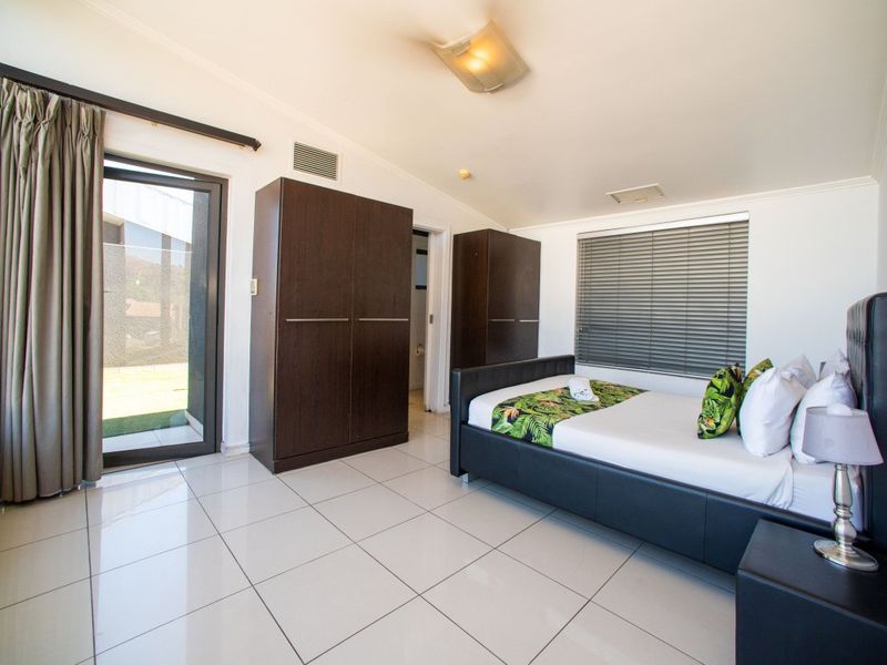 A bright bedroom featuring tiled flooring, built-in cupboards, and a sliding glass door providing direct access to the outdoor area.