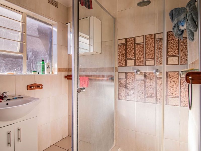 A functional bathroom featuring a vanity cabinet with basin, a glass-enclosed shower, and tiled finishes throughout.