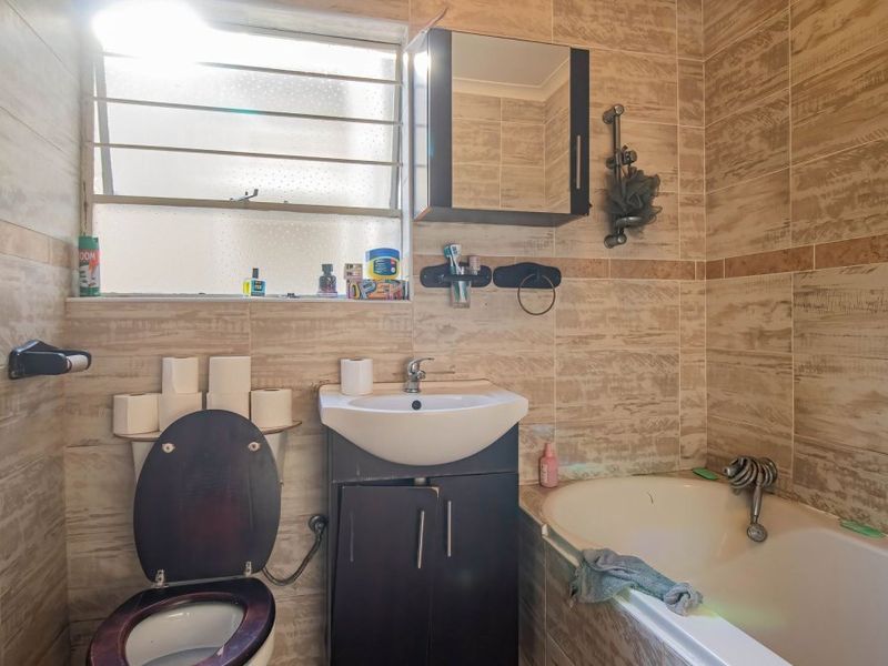 A functional bathroom featuring tiled walls, a vanity cabinet with a basin, a bathtub, and a toilet, providing essential amenities in a compact layout.
