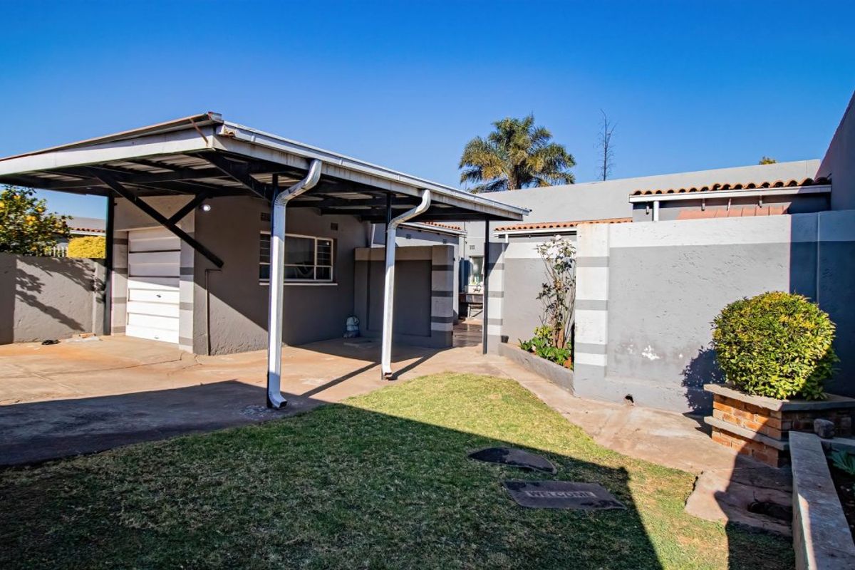 Rear exterior view of the property featuring a covered carport, garage access, paved driveway, and a small garden area with boundary walls.