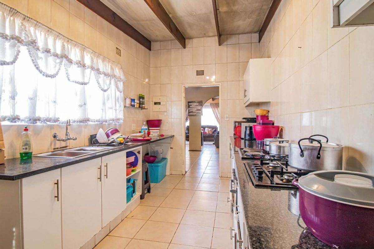 A functional kitchen featuring granite countertops, built-in cabinetry, a gas hob, and tiled finishes throughout, offering a practical layout for daily meal preparation.