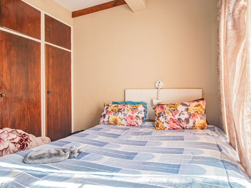 A compact bedroom featuring built-in wooden cupboards and an exposed timber ceiling beam, offering a functional space with potential for modernization.