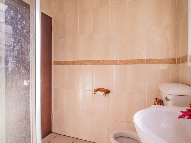 A functional bathroom featuring a shower enclosure, pedestal basin, and toilet with neutral wall tiling.