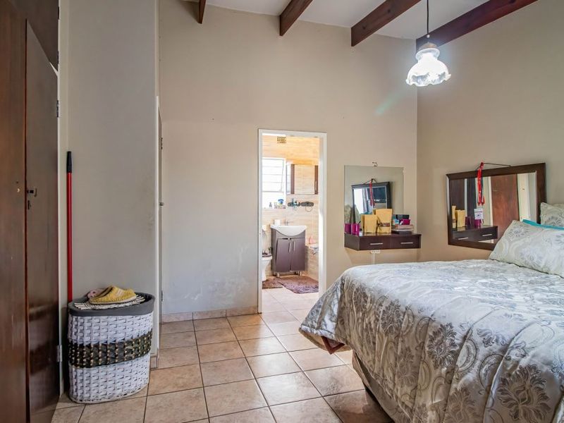 Spacious bedroom featuring exposed timber ceiling beams, tiled flooring, and direct access to an en-suite bathroom.