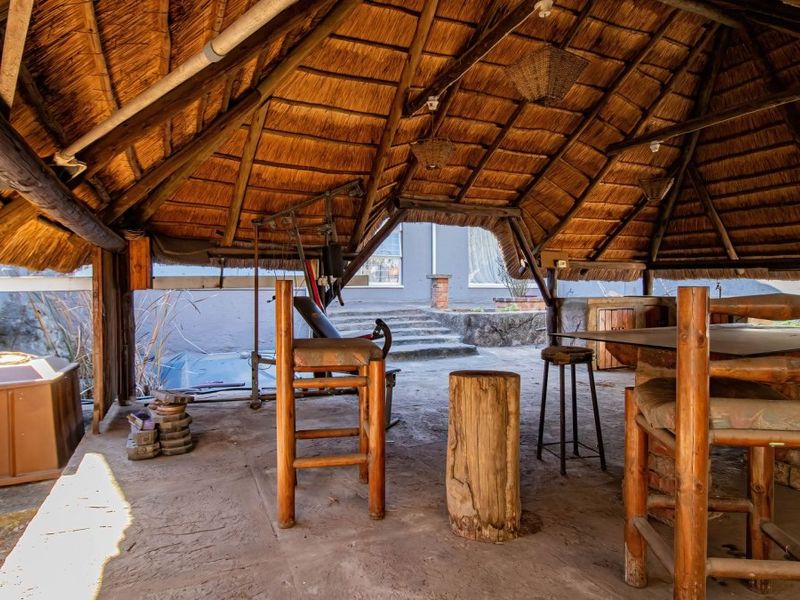 An outdoor thatched-roof entertainment area featuring a built-in masonry counter and concrete flooring, providing a rustic space for outdoor dining and relaxation.