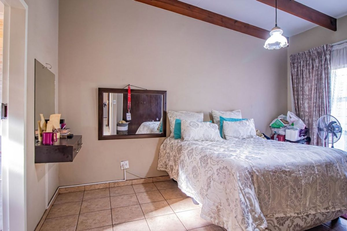 A bedroom featuring tiled flooring, exposed timber ceiling beams, and direct access to an en-suite bathroom through a sliding door.