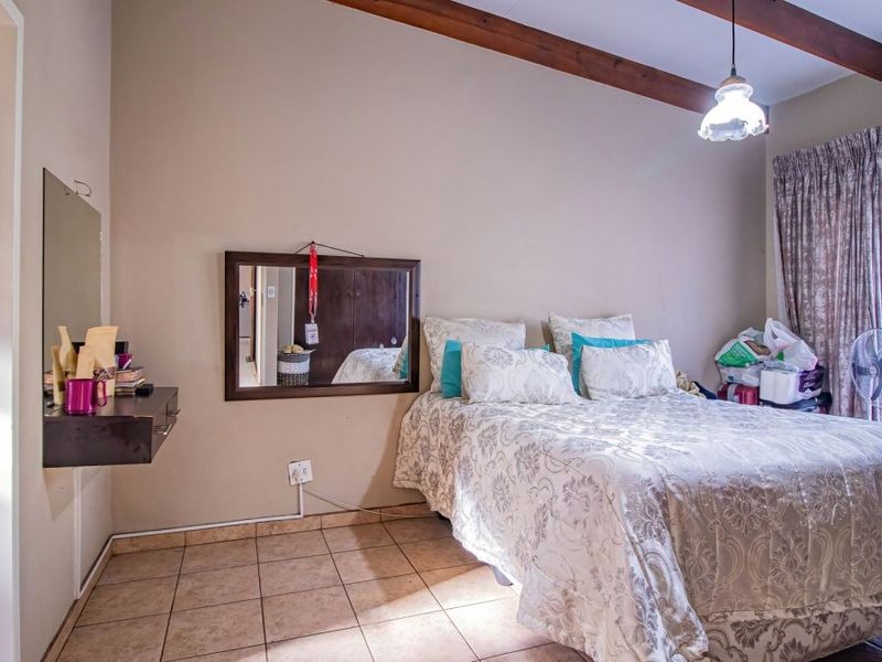 A bedroom featuring tiled flooring, exposed timber ceiling beams, and direct access to an en-suite bathroom through a sliding door.