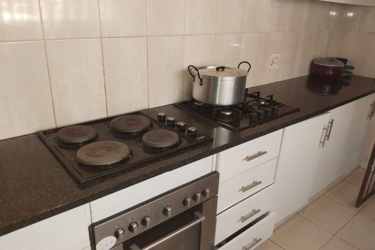 A functional kitchen featuring granite countertops, a combination of electric and gas hobs, a built-in oven, and white cabinetry with tiled backsplash.