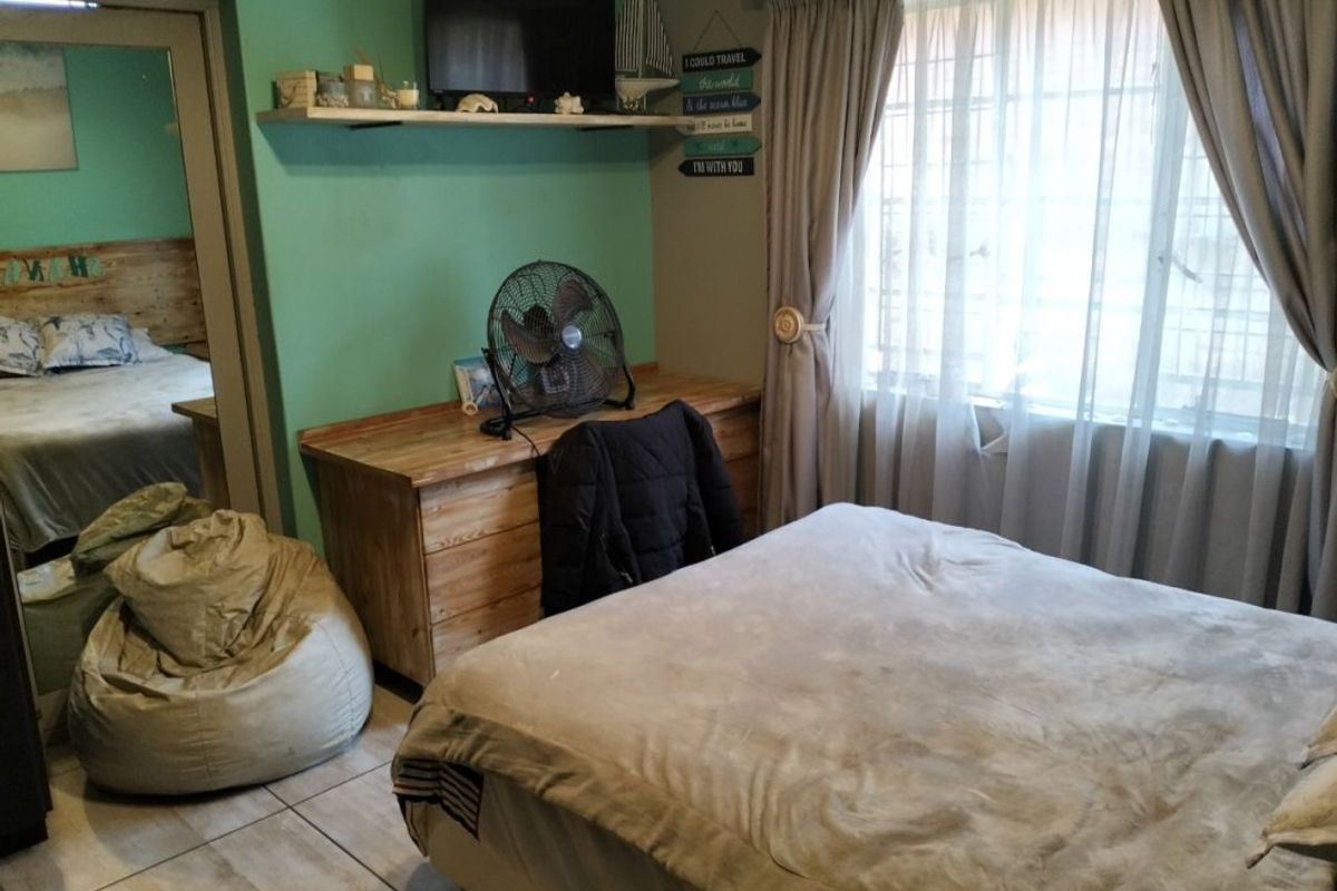 A bedroom featuring tiled flooring, a built-in wall shelf, and natural light through a window with curtain treatments.