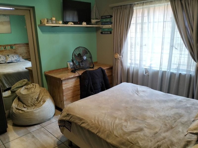 A bedroom featuring tiled flooring, a built-in wall shelf, and natural light through a window with curtain treatments.