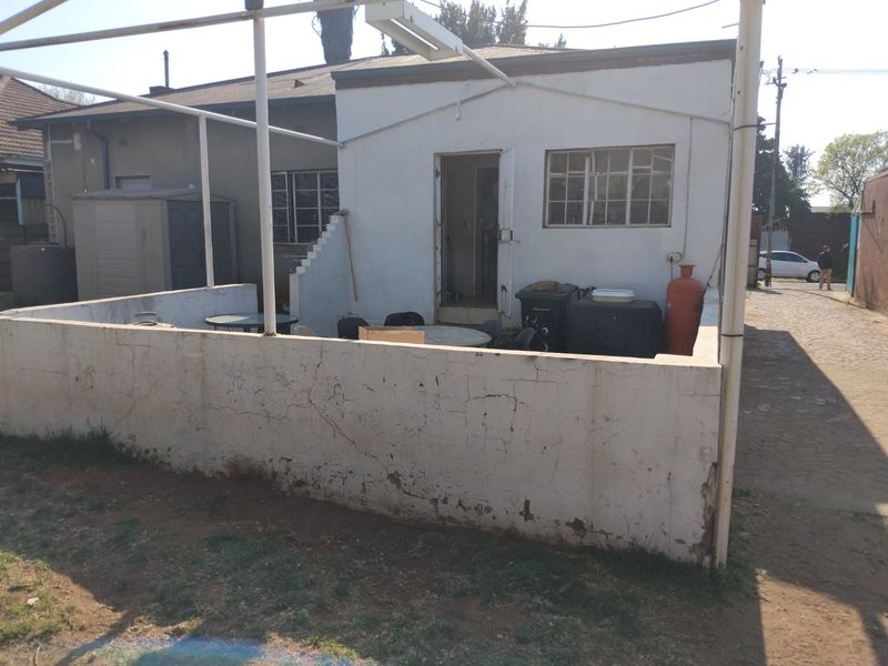 Rear exterior view of the property featuring a covered patio area with a low masonry wall and steel-framed windows.