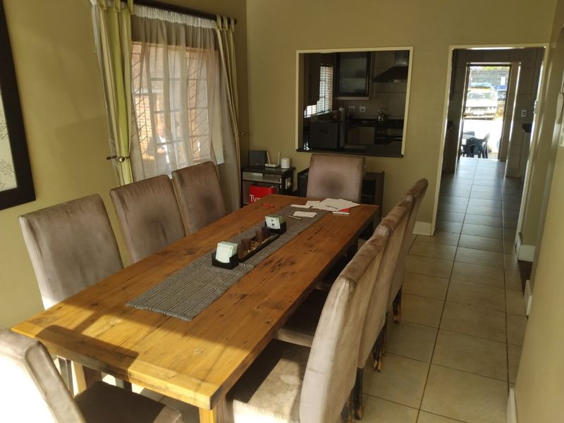 A dining room featuring tiled flooring and a serving hatch connecting to the kitchen, with natural light entering through a window with security bars.