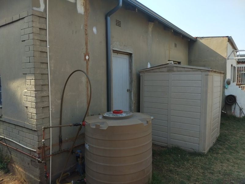 Rear exterior view showing a water storage tank, external plumbing, and unfinished wall plastering on the building facade.