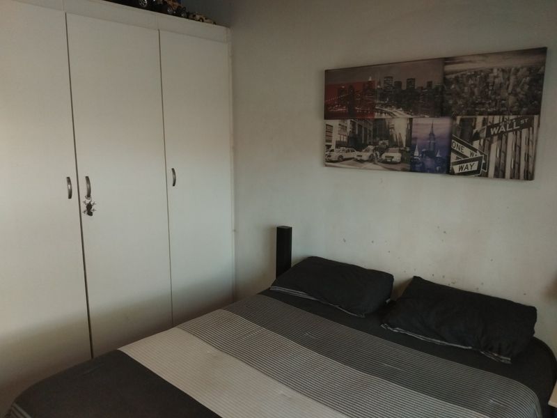 A bedroom featuring a white built-in wardrobe and visible wall surface wear, requiring cosmetic attention.