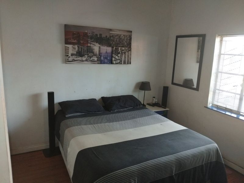 A bedroom featuring laminate flooring and a window with fitted blinds. The walls show visible signs of wear and require maintenance.