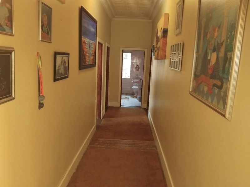 A central hallway featuring neutral walls, coving, and carpeted flooring, providing access to multiple rooms including a bathroom at the end.
