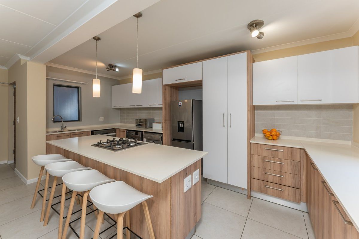 Modern kitchen featuring a central island with a gas hob, ample built-in cabinetry, stone countertops, and tiled flooring in an open-plan layout.