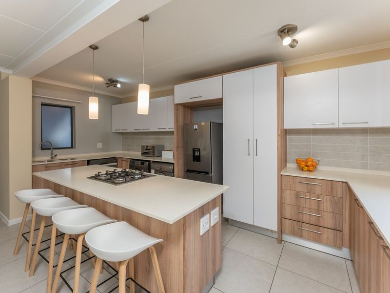 Modern kitchen featuring a central island with a gas hob, ample built-in cabinetry, stone countertops, and tiled flooring in an open-plan layout.