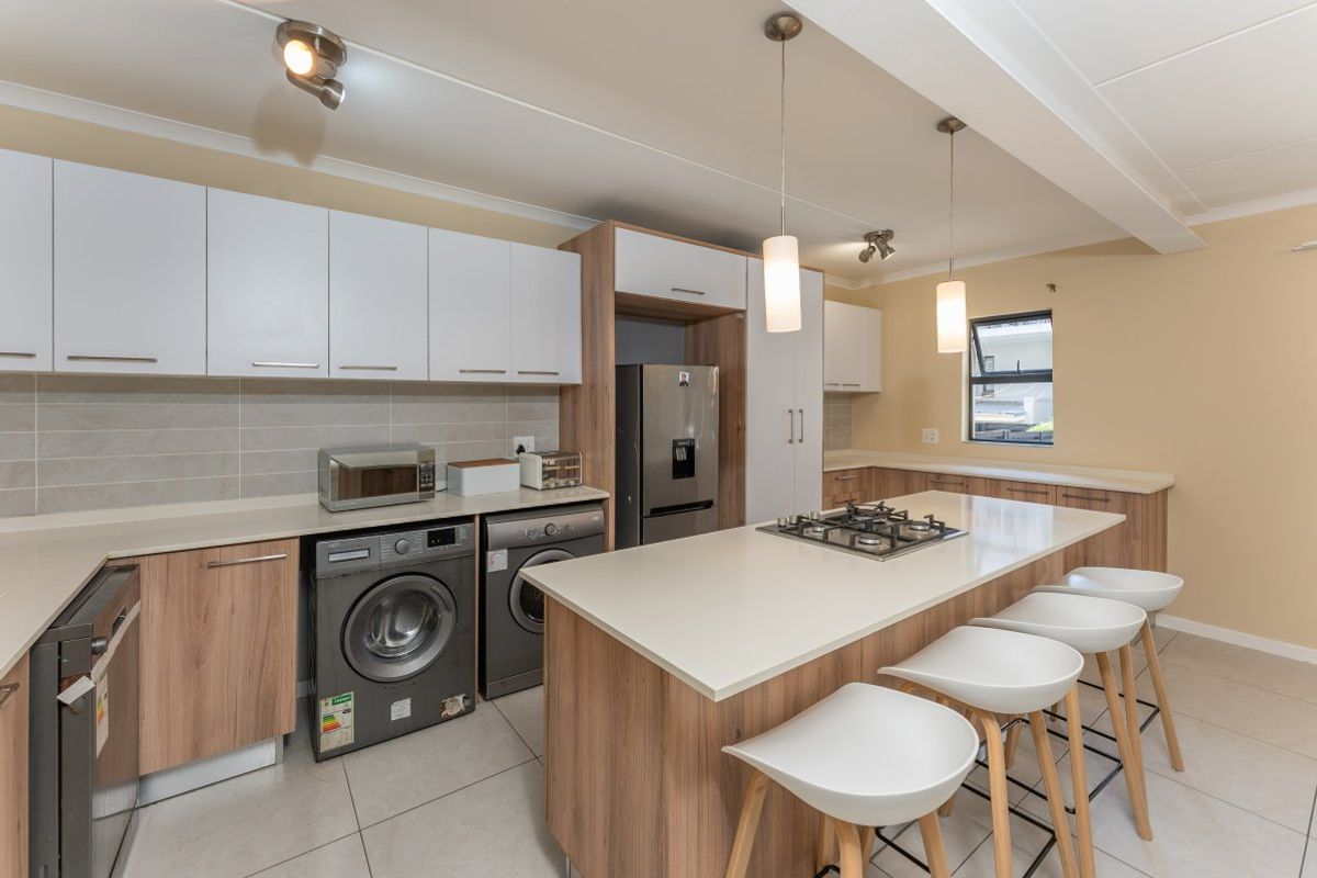 Modern kitchen featuring wood-finish cabinetry, stone countertops, a central island with a gas hob, and integrated appliance spaces.
